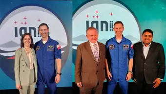 Zdjęcie przedstawia dwie grupy osób pozujących na tle logotypu „IGNIS” z kosmicznym motywem. Po lewej stronie kobieta w zielonym garniturze stoi obok mężczyzny w niebieskim skafandrze astronauty z logo Europejskiej Agencji Kosmicznej (ESA) i polską flagą na ramieniu. Po prawej stronie ten sam astronauta pozuje z dwoma mężczyznami w garniturach. Wszystkie osoby uśmiechają się.