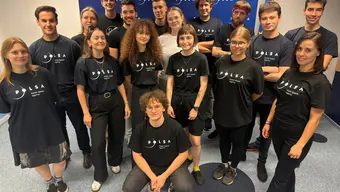 Zdjęcie grupy kilkunastu młodych osób w czarnych koszulkach z logo POLSA